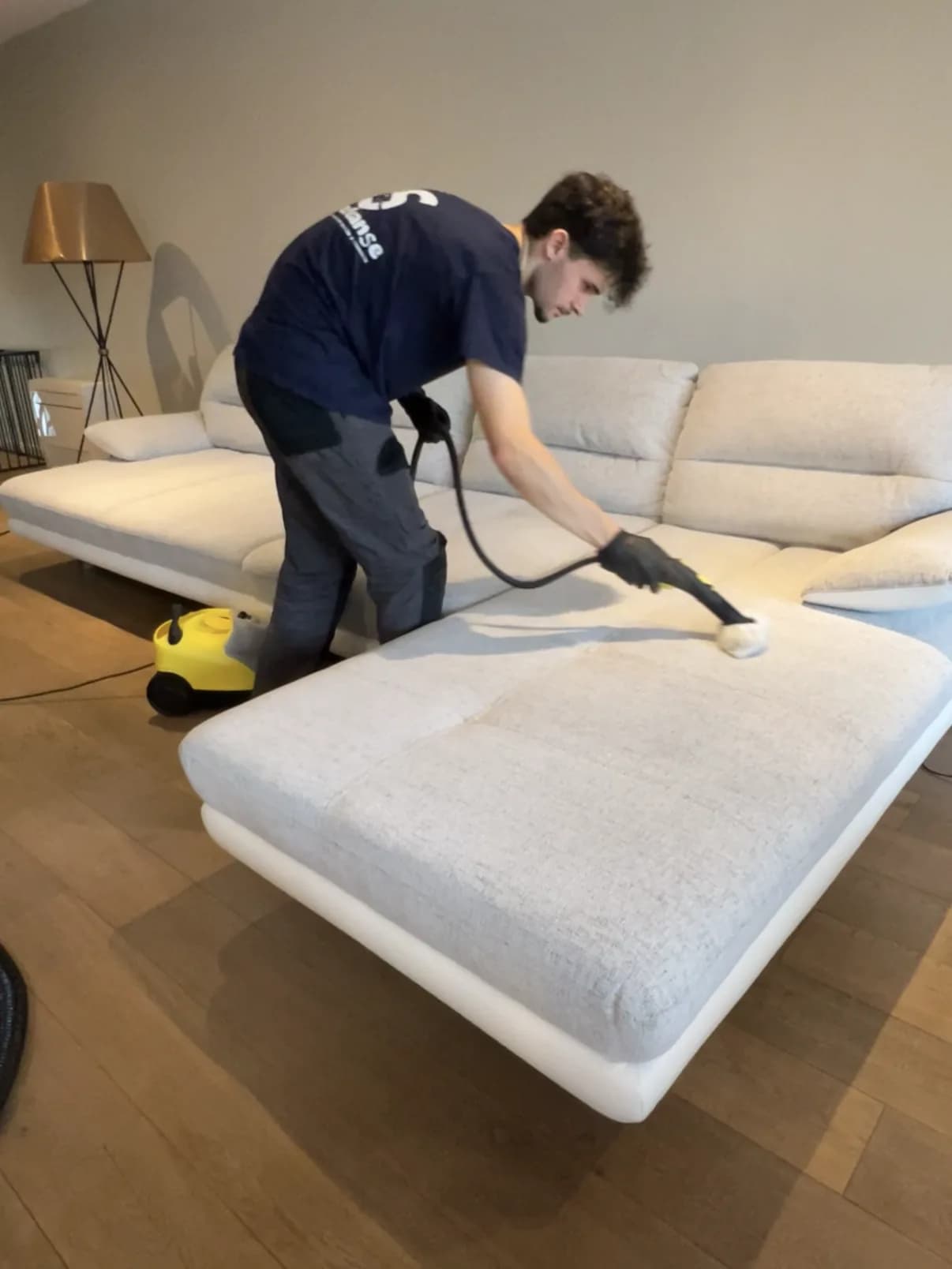 Intervenant SafeCleanse nettoyant à la vapeur un canapé d'angle en tissu clair, au domicile du client